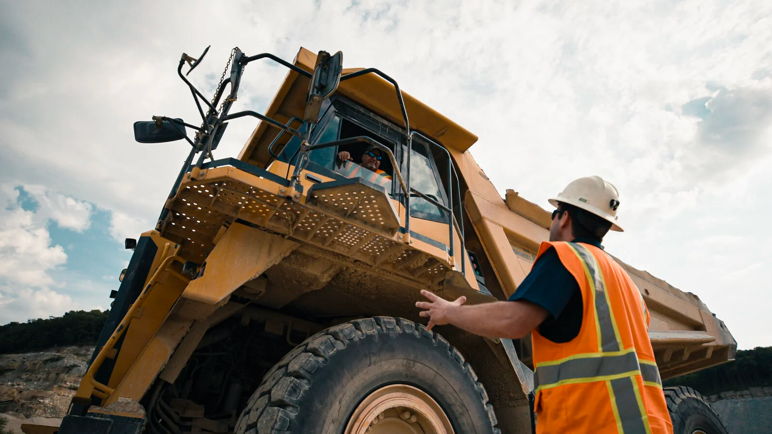 Construction workers coordinating beside a quarry haul truck